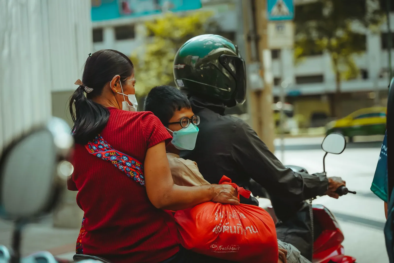A family of three riding a motor scooter on a Bangkok street