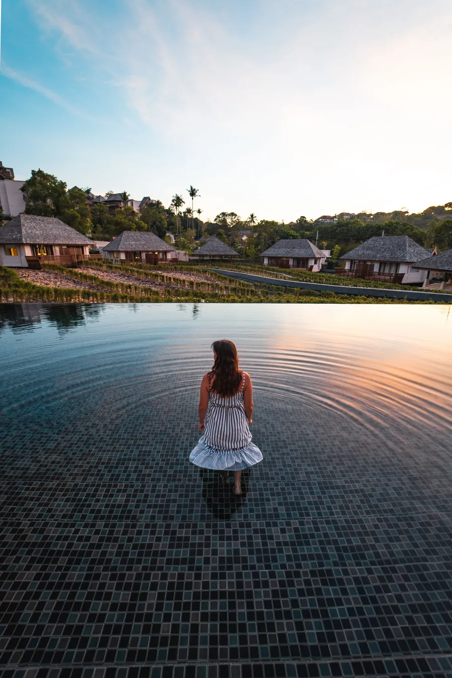 Traveler looking over an infinity pool toward resort cottages in Thailand