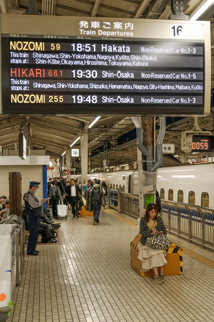 Commuters waiting on a Japanese train platform beside an electronic departure board
