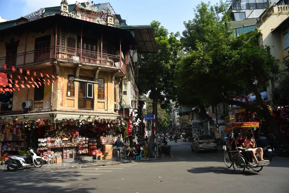 A street corner in Hanoi with traditional architecture and a passing rickshaw